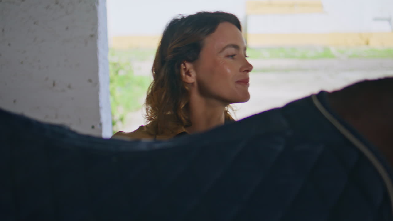 Woman rider putting saddle horse at paddock closeup. Jockey preparing stallion