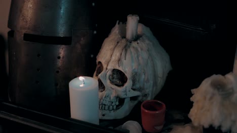 candle lit skull with wax drips beside medieval helmet, creating eerie ambiance