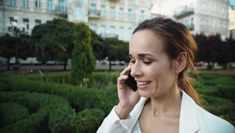 retrato de una mujer profesional sonriente hablando con un teléfono inteligente en un paseo por la ciudad.