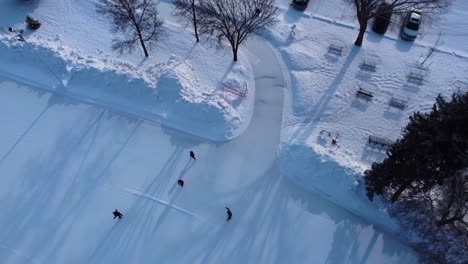 aerial-winter-flyover-drop-over-4-adults-skating-at-birds-eye-view-sunset-at-Canada's-largest-manmade-ice-skating-rink-at-Victoria-Park-arena-surrounded-by-tall-trees-headed-to-parked-cars-lot-ice3-3