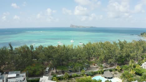 Aerial-view-showing-turquoise-colored-ocean-of-Mauritius,-Coin-de-Mire-and-driving-cars-on-coastal-road-during-sunny-day