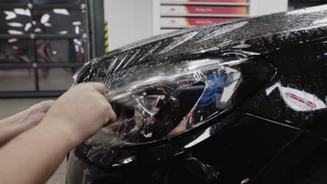 a worker installs a custom clear bar, paint protection film to the front of a black car