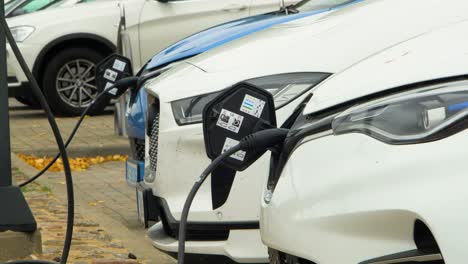 three electric cars charging on a city street, a cable connected to a car, future of the automobile, clean sustainable energy, overcast day, medium shot