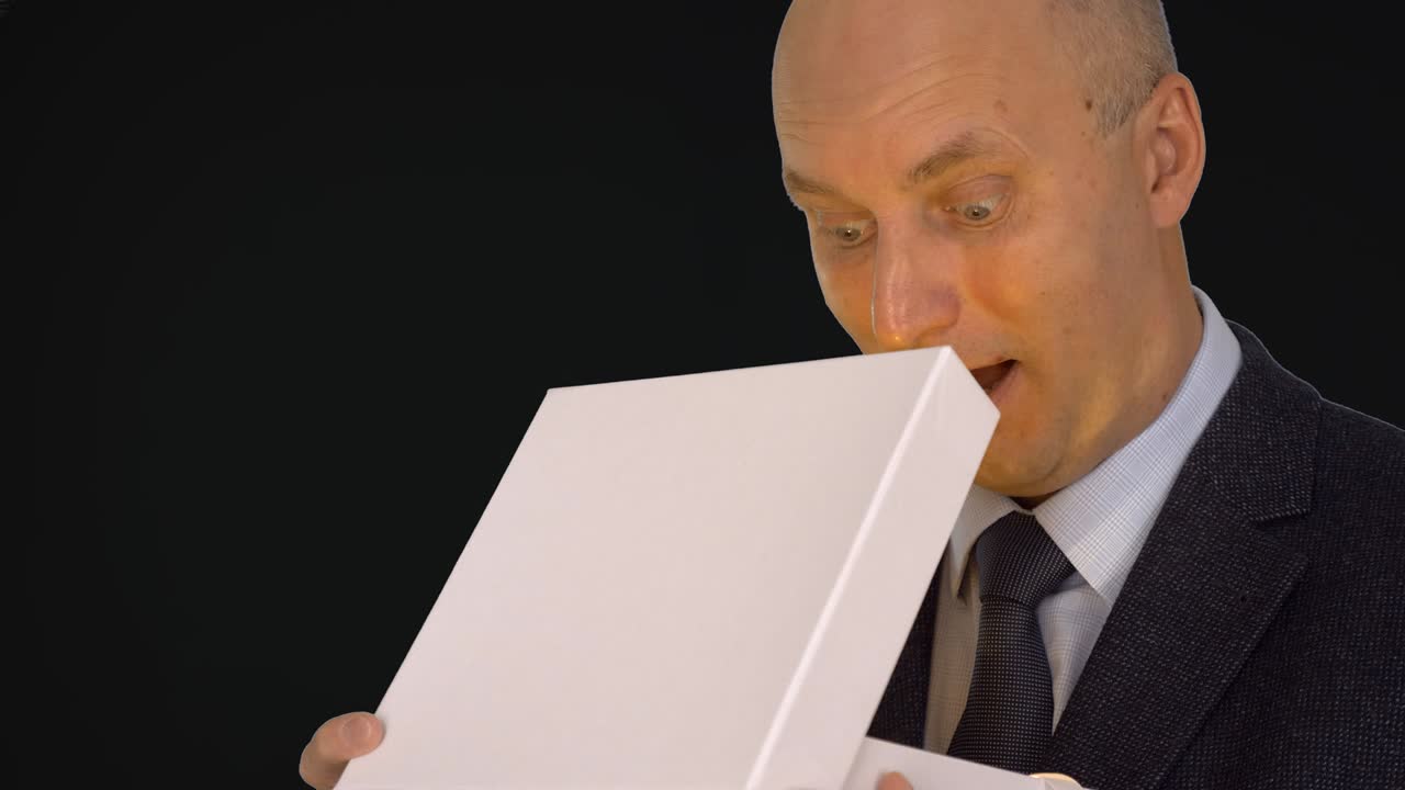 Adult caucasian man in classical formal suit open white gift box. Man looking into gift box and spot light at his face. Alpha channel chroma key transparent background. Can place text or logo on box.