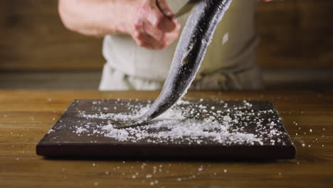 man uses knife to clean herring from salt on wooden board