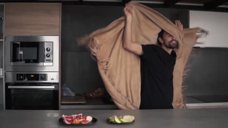 Joyful-man-prepared-healthy-breakfast-at-kitchen-at-home-while-dancing-and-making-fun-covered-with-plaid