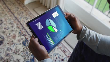 hands of caucasian man sitting on sofa, using tablet with statistics on screen