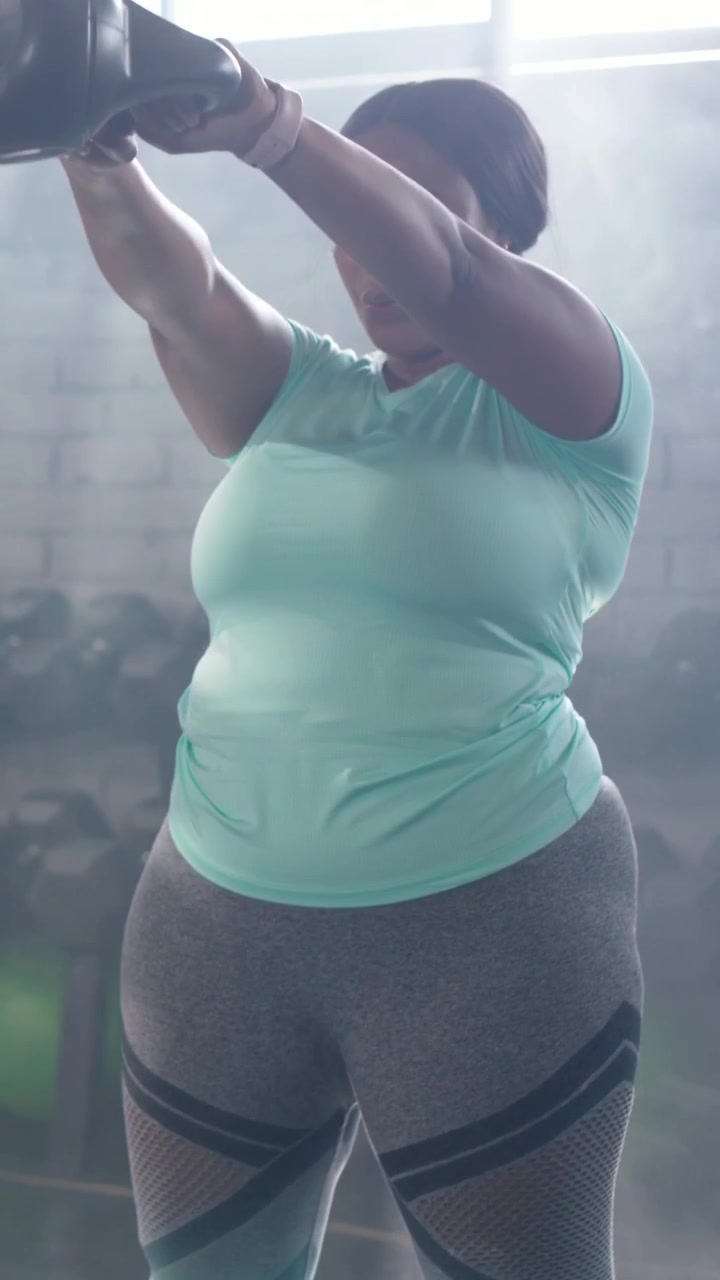 Video verticale: Donna in top color menta che si piega, afferrando un kettlebell da 5 kg e facendolo oscillare per allenare la forza in palestra