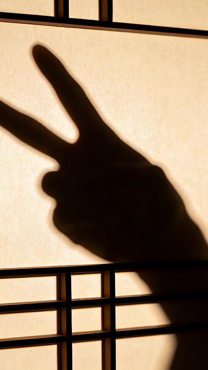Vertical video: Hand shadow making V gesture, shifting on shade at window with warm backlight