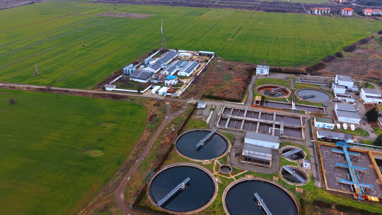 Wide aerial shot of water purification facility and fields. Elevated view showing a sewage treatment plant integrated into a rural landscape with agricultural fields
