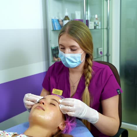 beautician cleans woman's face before a cosmetic procedure with napkins. video from the top