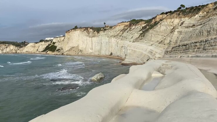 Static wide shot of the Stair of the Turks (Scala dei Turchi) in Sicily on a bright, sunny day. The striking white limestone cliffs contrast beautifully with the deep blue Mediterranean Sea and clear