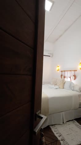 interior of a clean hotel room with a bed headboard textile with white sheets and pillows, macrame rugs seen from a slightly open door closing