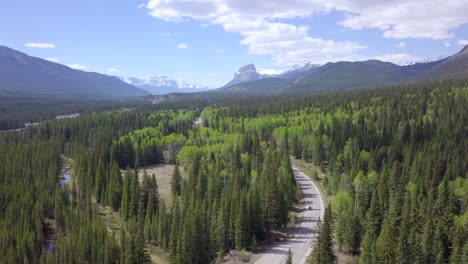 motorcycle driving by in dreamlike snow covered mountain tops and green spruce forest area in canada, aerial