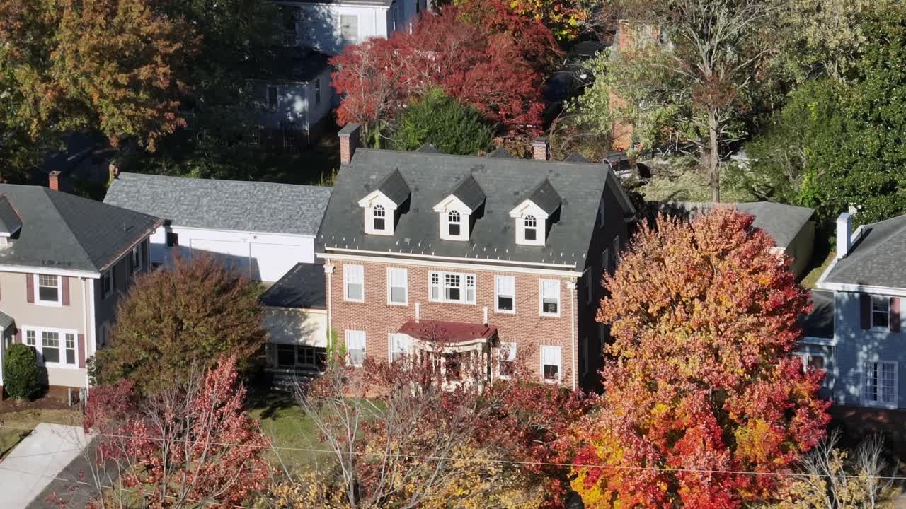 Sweeping drone footage over a picturesque American suburb during peak autumn reveals neat houses, tree-lined streets, and a patchwork of crimson, gold and orange foliage under bright midday light