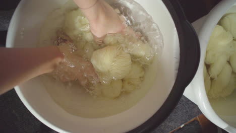 top-down view of hands reaching into a bucket to hand-mix yarn