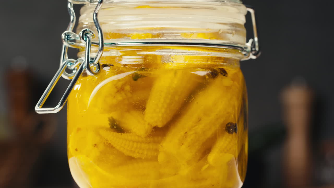 Close-up of fermented yellow mini corn with black pepper in can. Preservation of vegetables in glass jars. Fermentation preserved mini corns with spices.