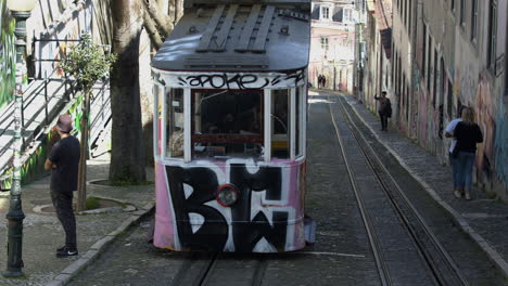a portuguese man taking video of an electric train coming down on the railroad in calcada da gloria, lisbon, portugal - medium shot