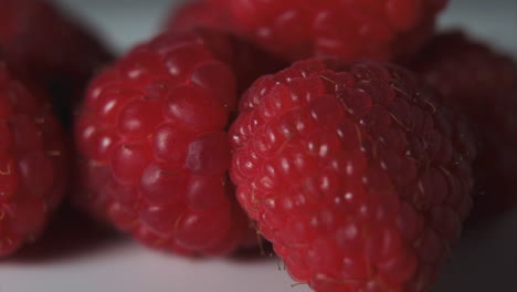 Panning-group-of-raspberries-on-white-plate-with-black-background