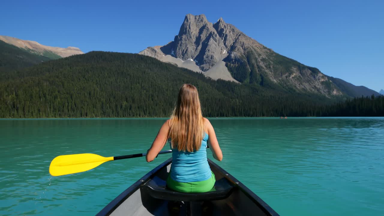 vista trasera de una joven mujer caucásica remando en un barco en un río turquesa en el sol 4k