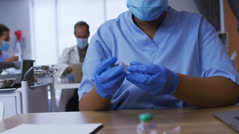 African-american-female-doctor-wearing-face-mask-inspecting-vial-of-covid-vaccine-in-hospital