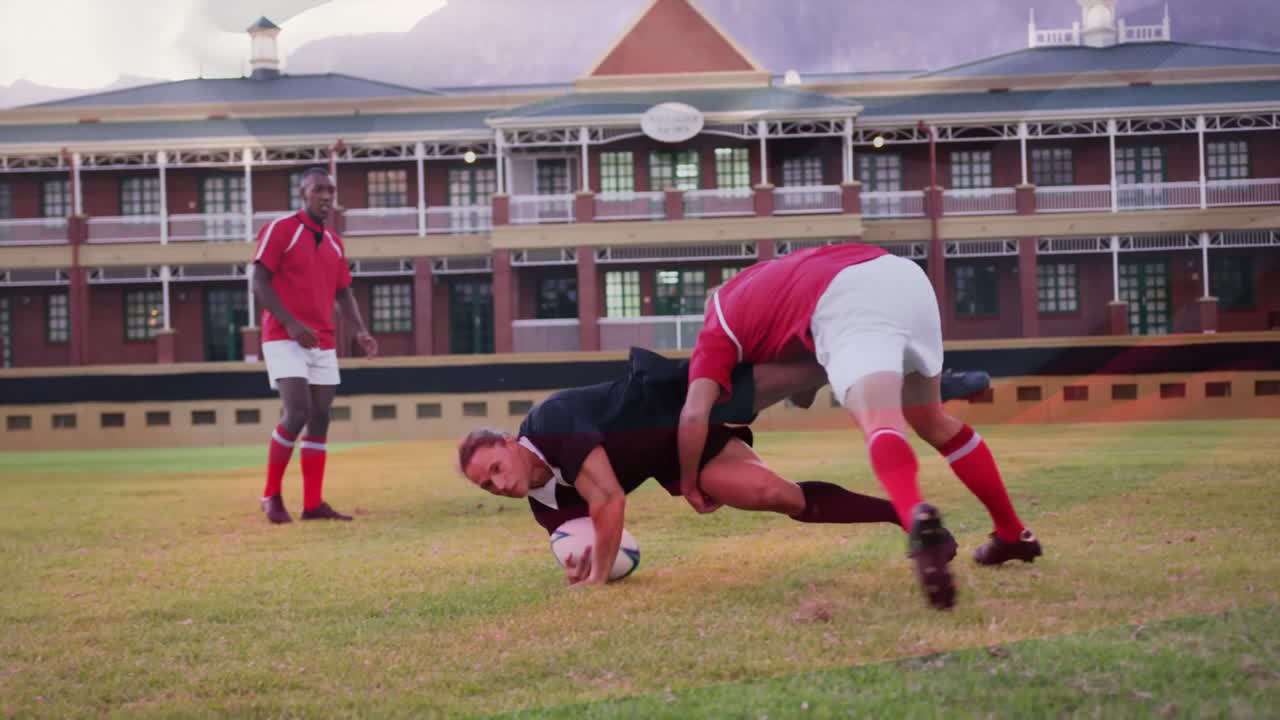 Tackling on grassy field, rugby players in front of large brick building