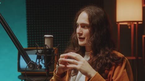 young podcast host with long curly hair talking in mic in recording studio