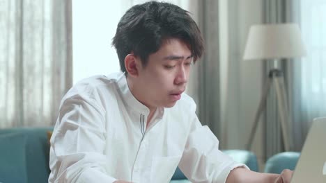 close up of asian man student rub his eyes while typing on computer at home