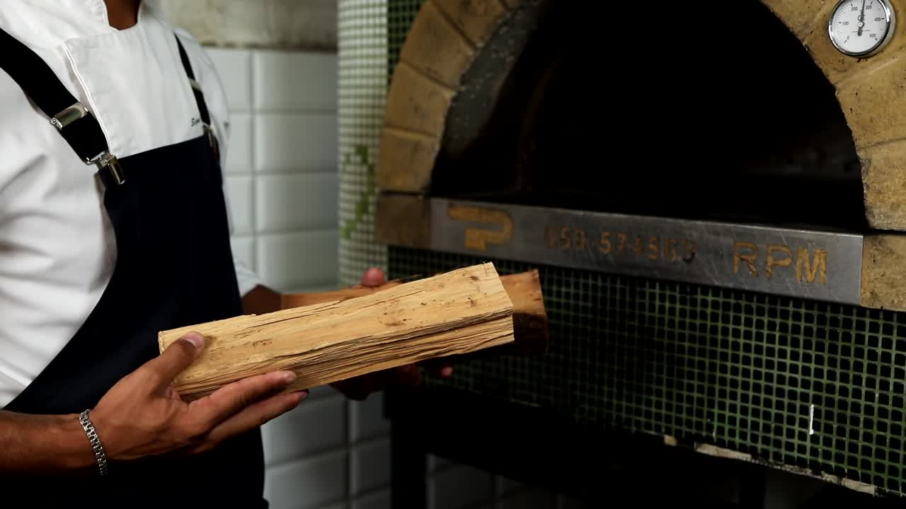 요리사 가 피자 오븐 에 나무를 로딩 하고 있다