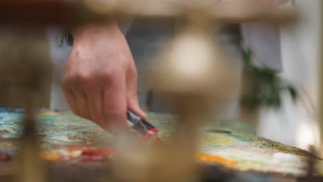 artist squashes paint out of tube in studio closeup. mature man prepares crimson acrylic shade for artwork in shop. painter works with colors