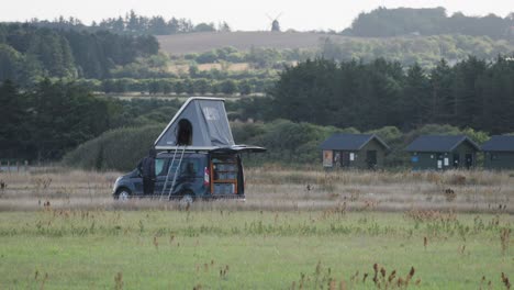 a custom-built camper van with an open tent on the roof is parked in the field