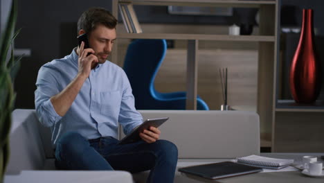 corporate man calling phone looking tablet research business data in home office