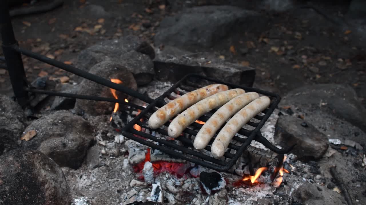 salchichas a la parrilla bratwursts en red de parrilla sobre fuego de campamento abierto