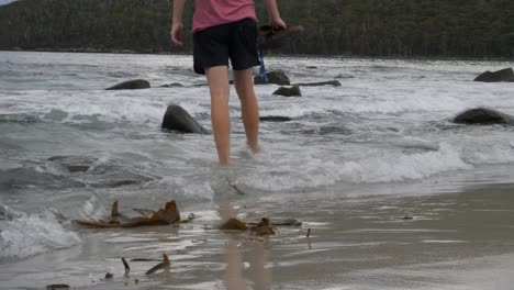 slow motion of person in shorts walking into water with rocks and rolling waves, tasmania, australia