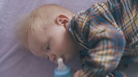 cute boy eats milk mix from bottle on bed with pink plaid