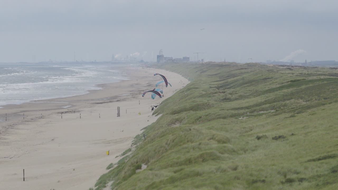 Una telecamera professionale si muove da sinistra a destra, creando un effetto parallasse tra le dune in primo piano e il lontano Mare del Nord.