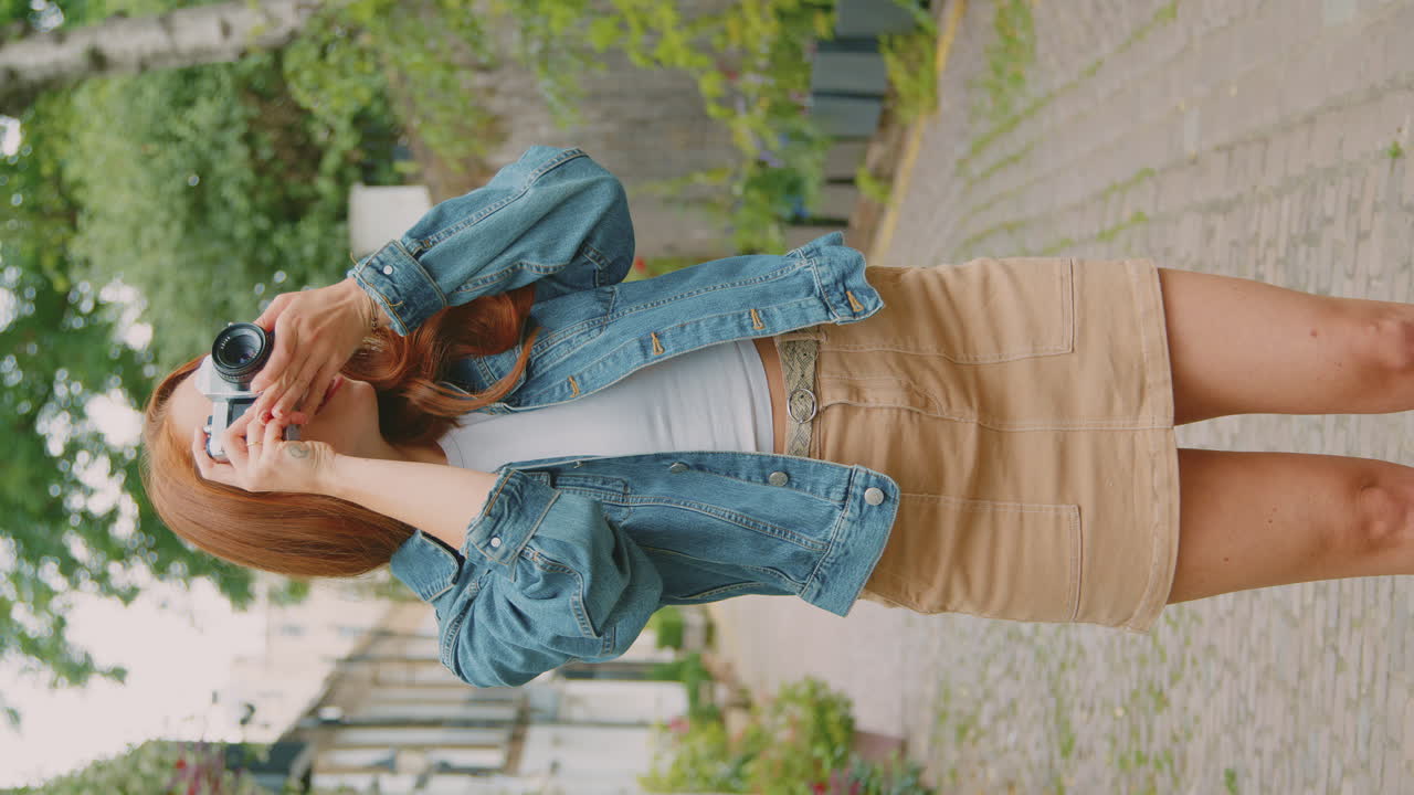 video vertical de una mujer joven en la ciudad tomando una foto en una cámara digital para publicarla en las redes sociales