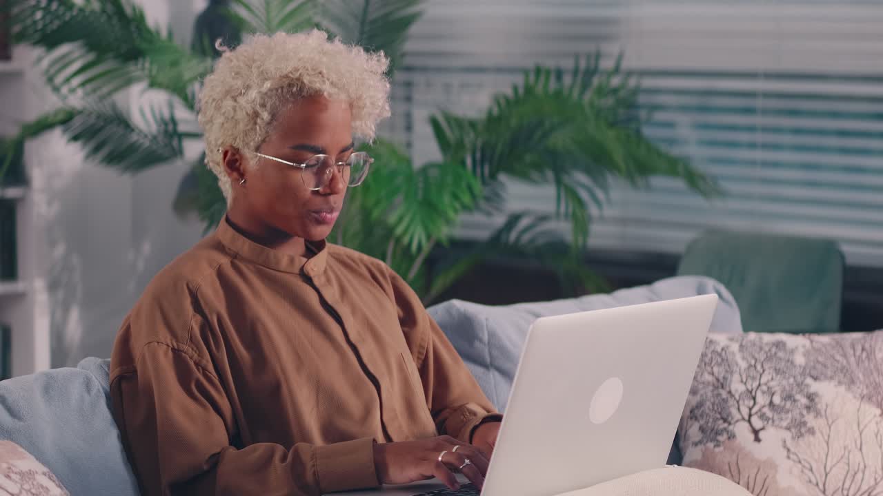 Concentrated afro american woman sit on sofa busy working on laptop browsing web