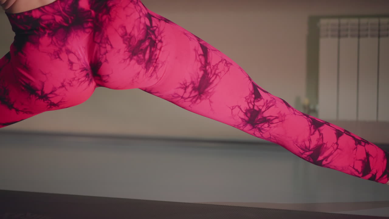 Wanita kulit putih melakukan peregangan kaki dinamis di atas matras yoga, dengan energi latihan tari mengenakan legging pink cerah dan atasan hitam, urutan split samping dan jangkauan, close-up sudut rendah pada kaki yang menunjuk.