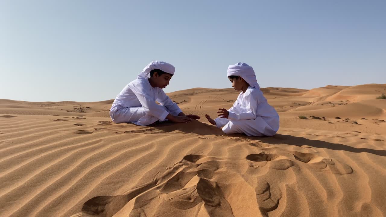 dos niños emaratíes jugando con arena en el desierto