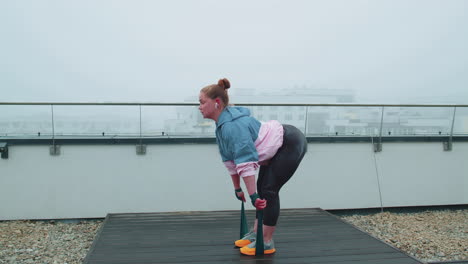 sporty girl in sportswear does yoga stretching exercising using rubber band on roof of house outdoor