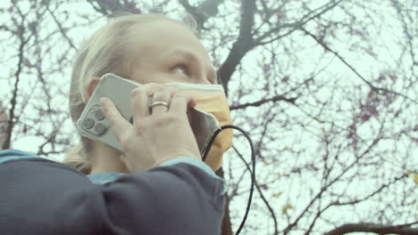 frau in maske spricht mit smartphone im park