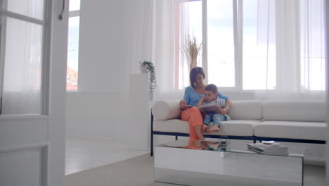 madre amorosa enseñando a su hijo a leer sosteniendo un libro hablando en el sofá en casa