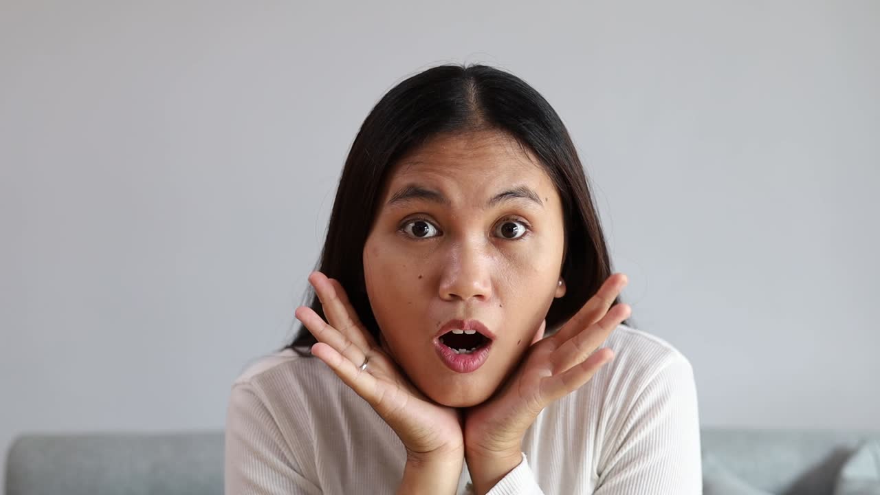 Young Asian woman at home raising eyebrows and opening mouth with surprise after seeing something unexpected