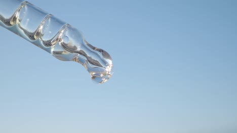 close-up of a dropper with a drop of clear liquid against a blue sky background