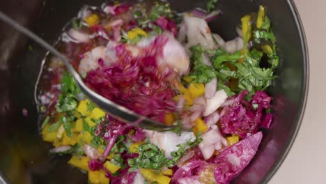 chef prepares cebiche by spooning ingredients into bowl