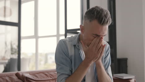 suffering middle aged man having headache while sitting on sofa at home