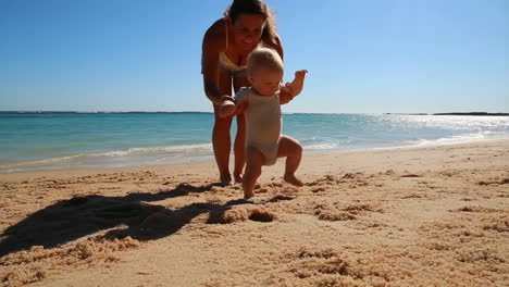 mother helps baby take first steps on the beach