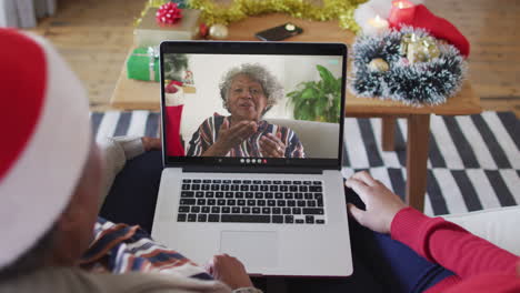 madre y hija afroamericanas usando una computadora portátil para una videollamada de navidad con una mujer en la pantalla