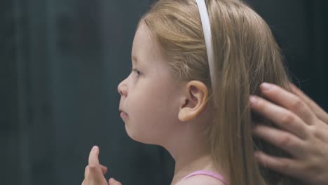 mother strokes little girl fixing long hair in bathroom